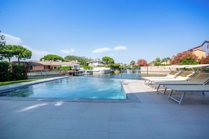 A swimming pool with a tiled deck, lounge chairs, and a clear sky.