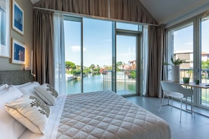 Quarto de hotel com uma cama grande, uma escrivaninha e vista para uma piscina e edifícios.