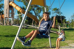A child on a swing in a park with a playground structure in the background. - Villa with all comfort (Albarella)