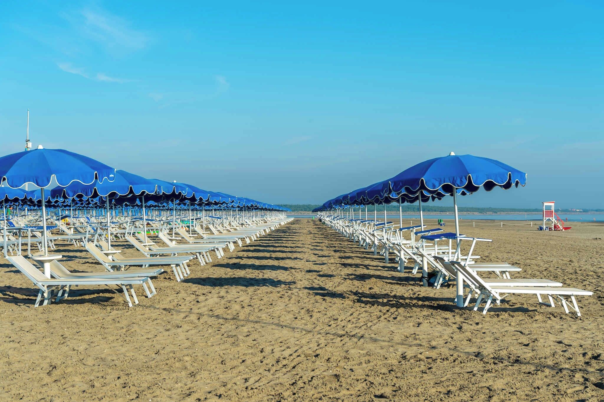 A beach with rows of sun loungers and blue umbrellas.