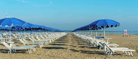 Uma praia com cadeiras de sol e guarda-sóis azuis.