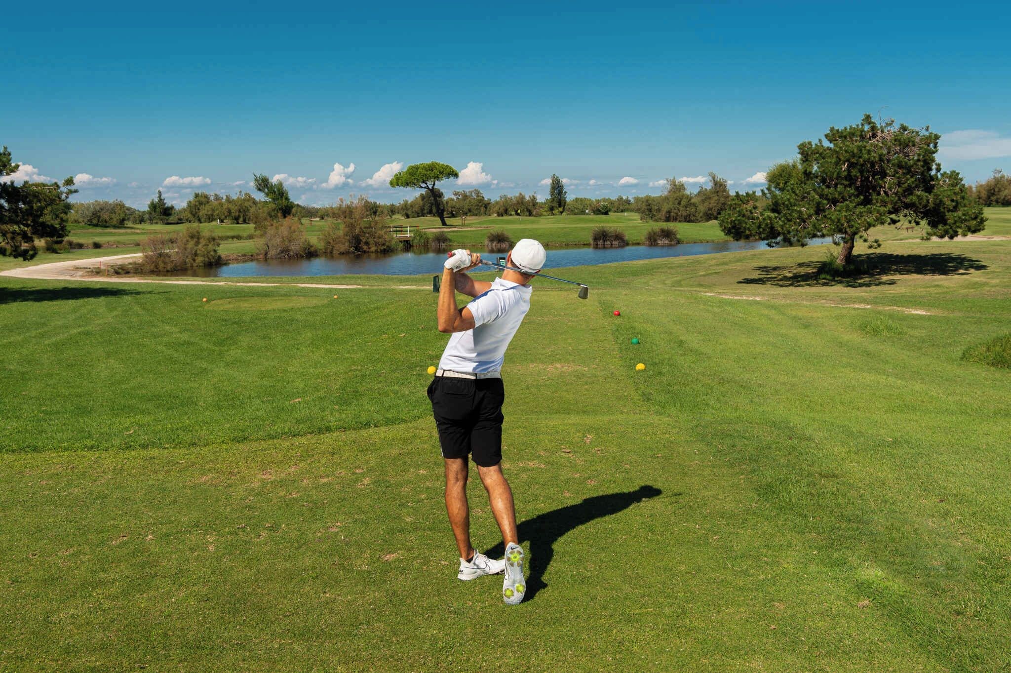 En person som spelar golf på en välskött golfbana med en vattenyta i bakgrunden.