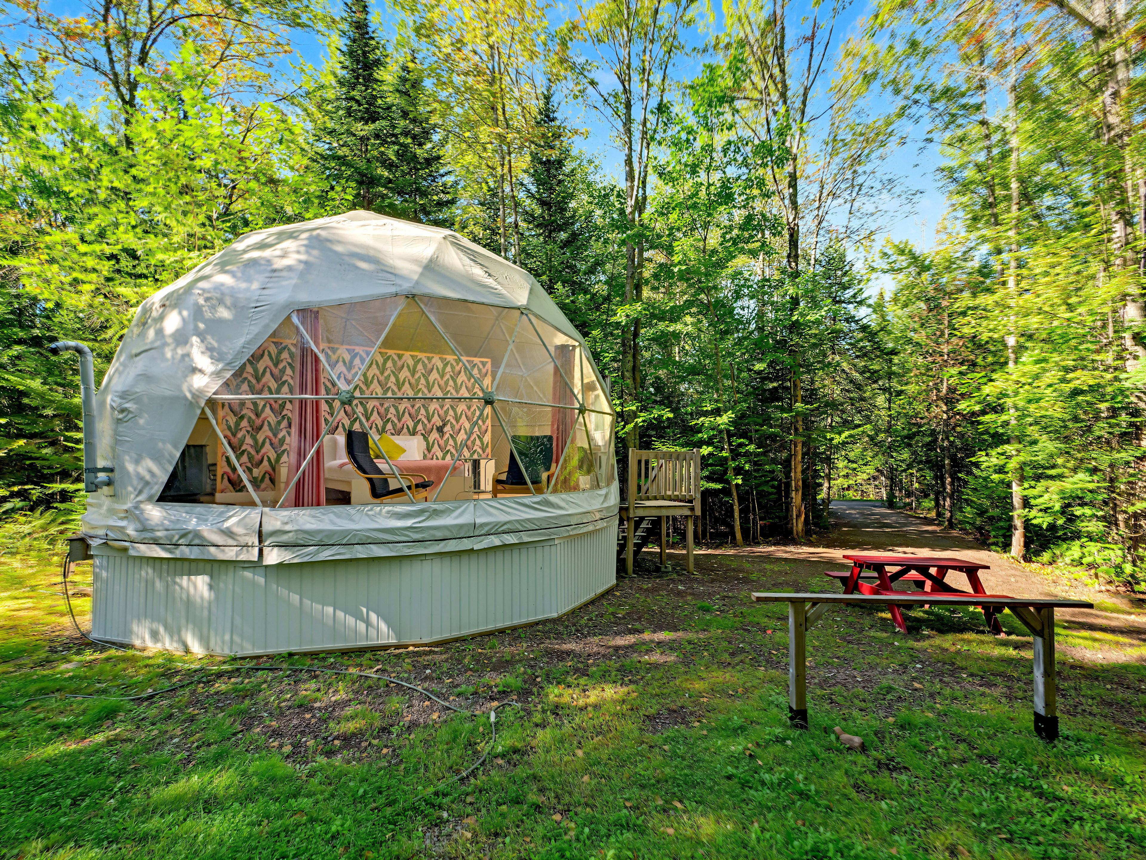 A dome-shaped tent with a bed and seating area, surrounded by a forest.