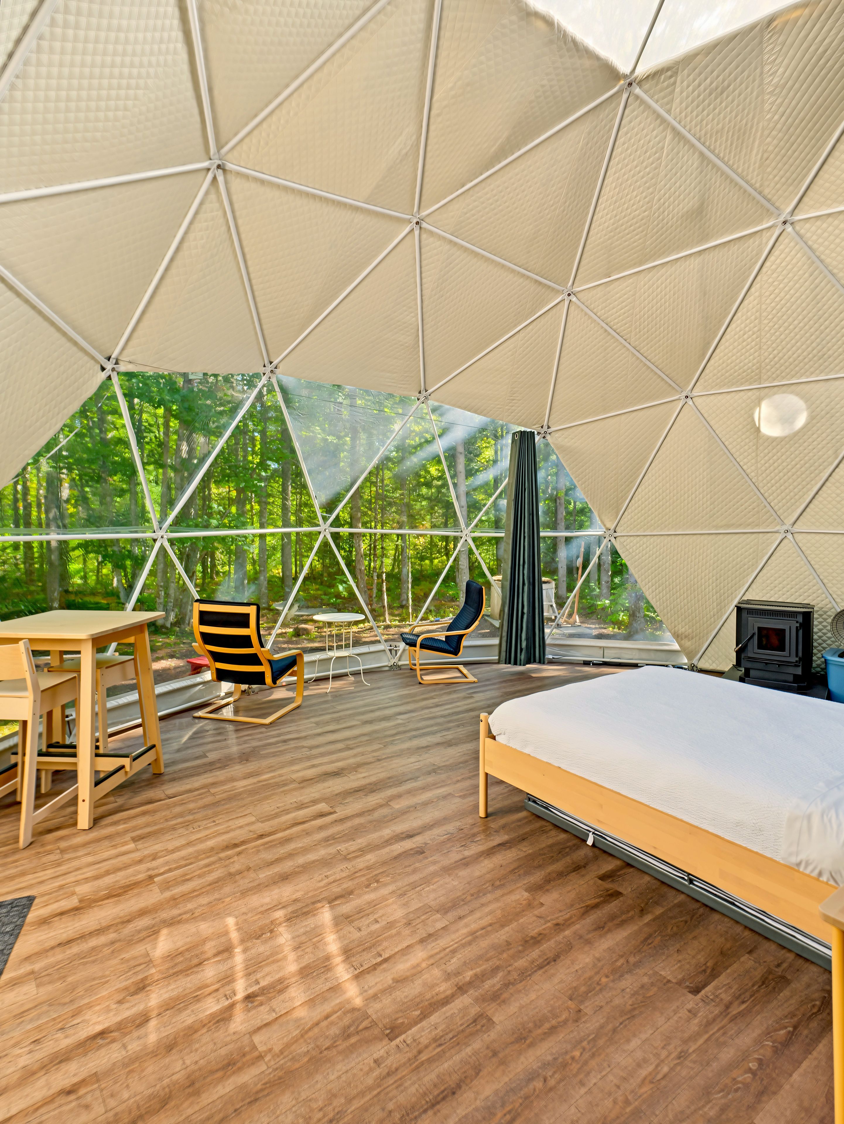 A tented accommodation with a bed, seating area, and a wood-burning stove.