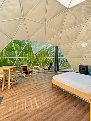 A tented accommodation with a bed, seating area, and a wood-burning stove. - Glamp Camp (Waterborough)