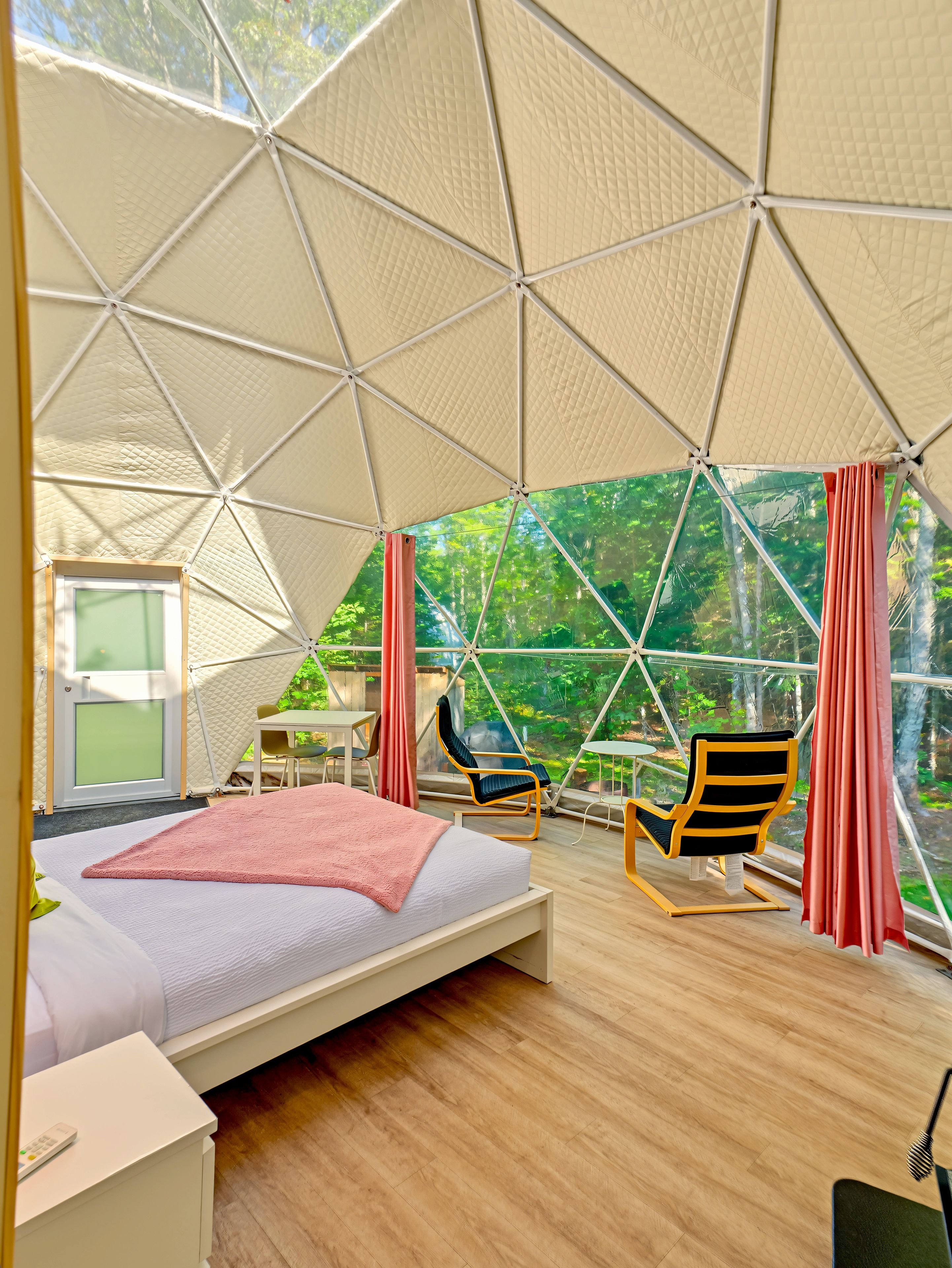 Habitación tipo tienda de campaña con cama, dos sillas, una mesa y vistas a la vegetación exterior.