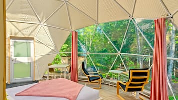 Habitación tipo tienda de campaña con cama, dos sillas, una mesa y vistas a la vegetación exterior.
