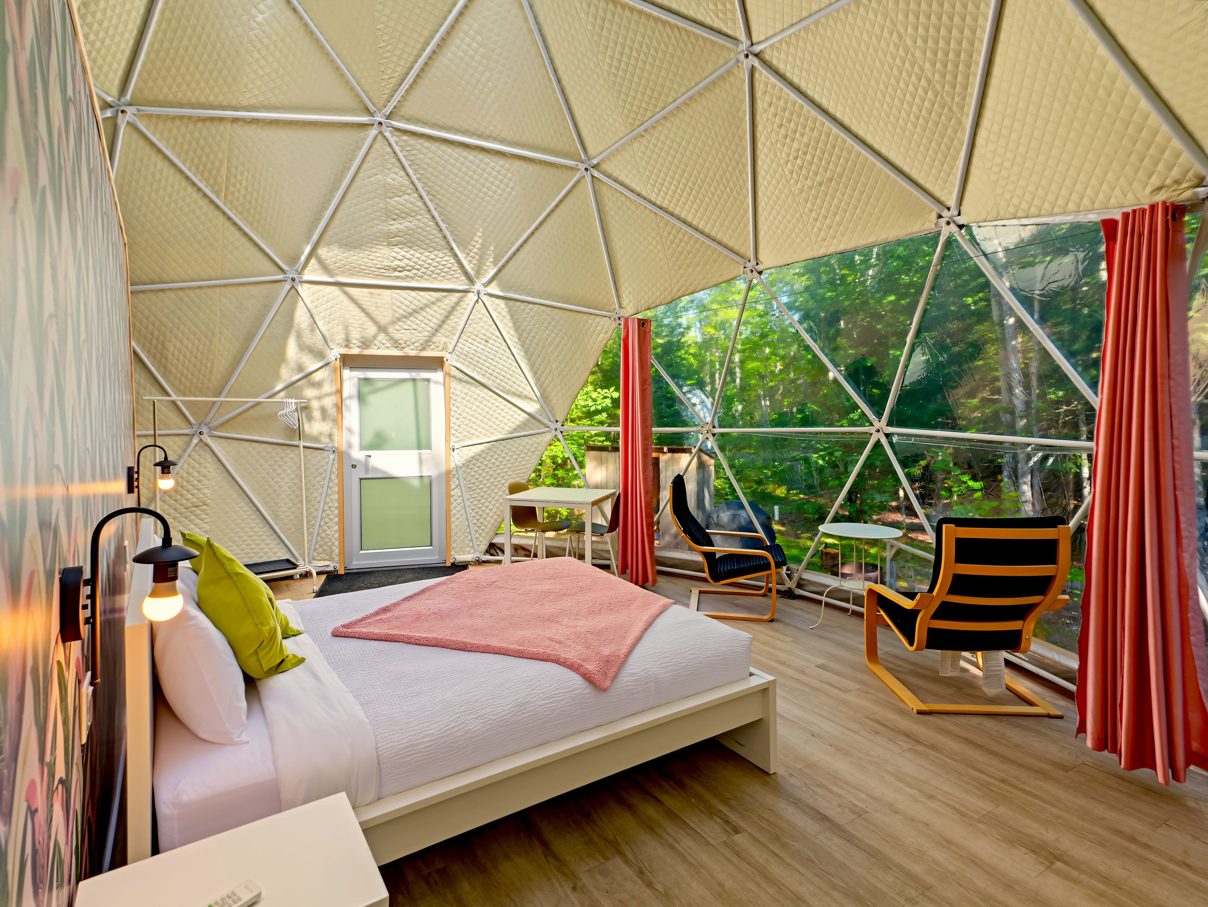 Een ruime tent met een bed, zithoek en uitzicht op groen.