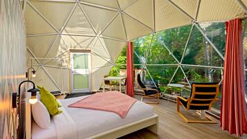 Een ruime tent met een bed, zithoek en uitzicht op groen.