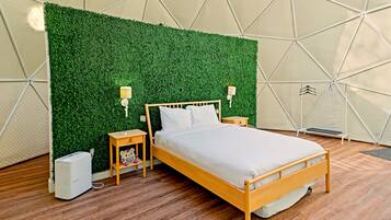 Een bed met houten frame en witte beddengoed, een groene muur met een geometrisch patroon, twee nachtlampjes en een klein nachtkastje met een lamp.