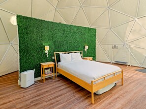 A bed with a wooden frame and white bedding, a green wall with a geometric pattern, two bedside lamps, and a small bedside table with a lamp. - Glamp Camp (Waterborough)