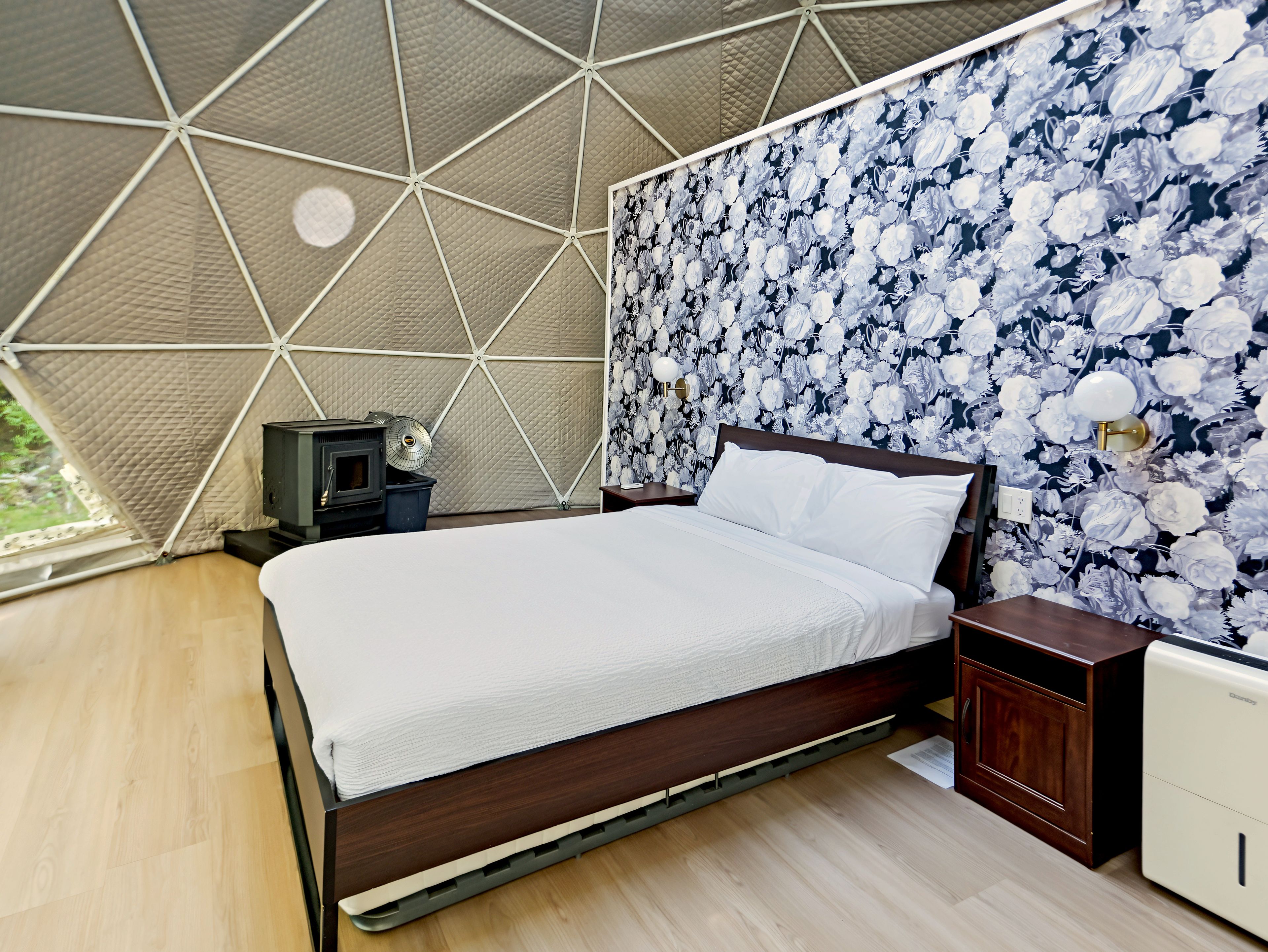 A bedroom with a bed, a nightstand, a dresser, a heater, and a wall with a floral pattern.