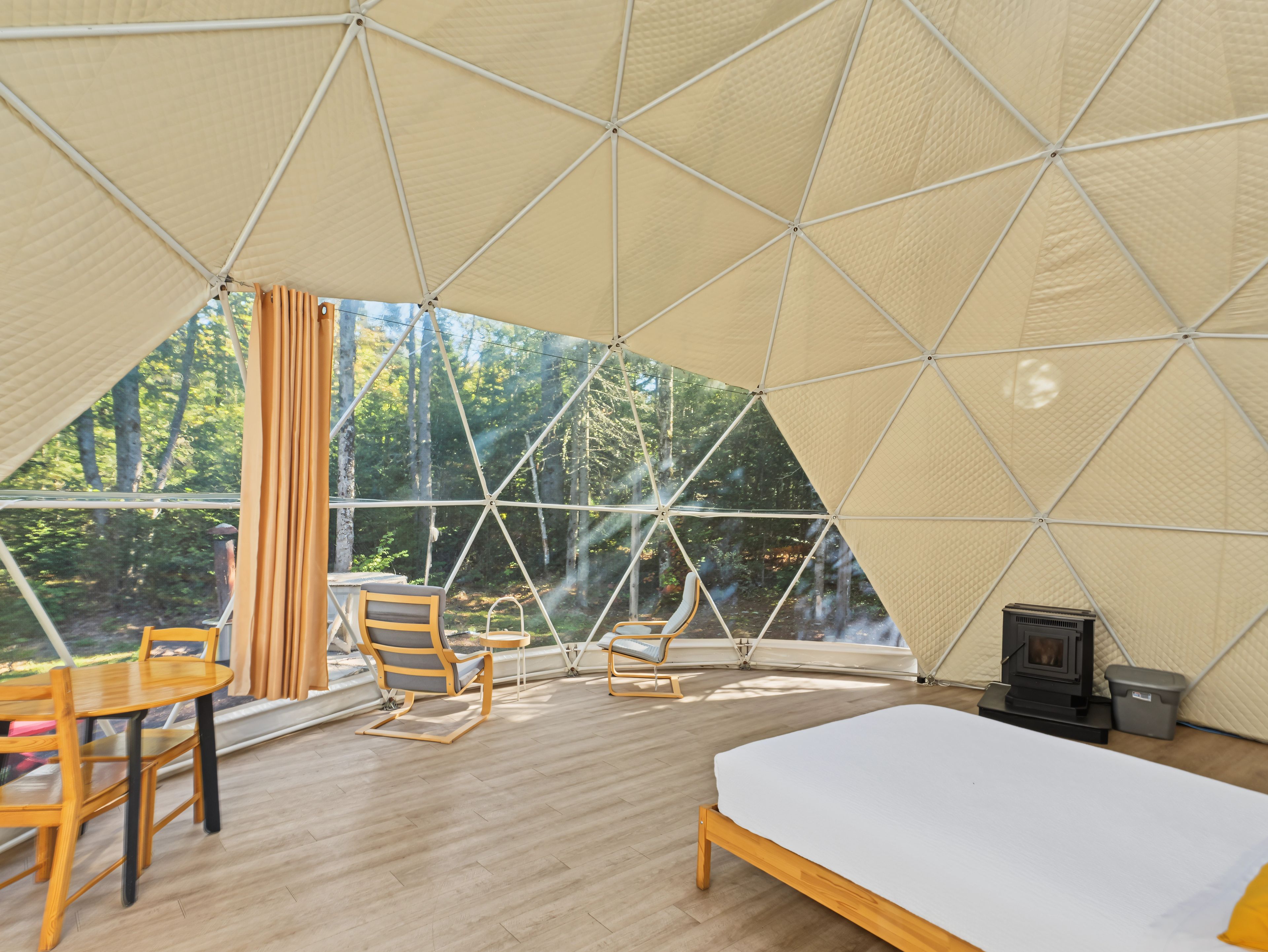 A tented accommodation with a bed, seating area, and a wood-burning stove.
