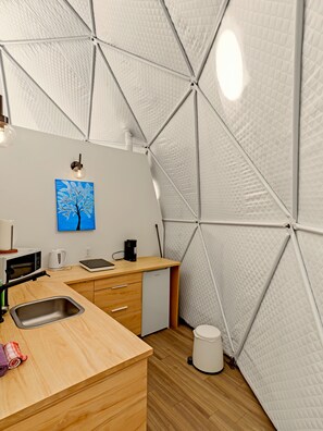 A compact kitchen with a microwave, kettle, and coffee maker on a wooden countertop. - Glamp Camp (Waterborough)