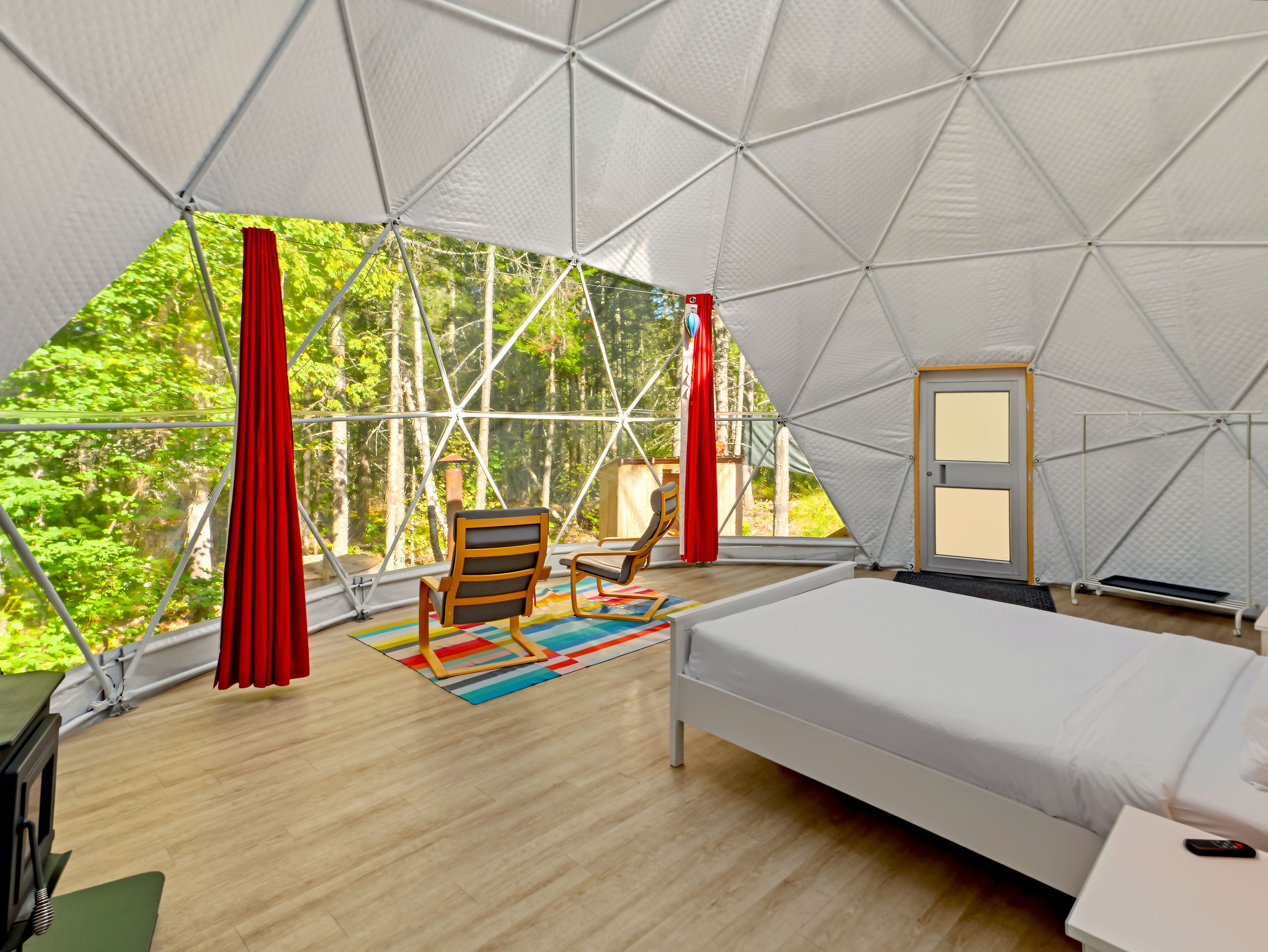 A geodesic dome room with a bed, a chair, and a view of greenery.
