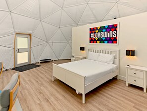 Una habitación tipo tienda de campaña con una cama, mesitas de noche, una lámpara de pared y una puerta.