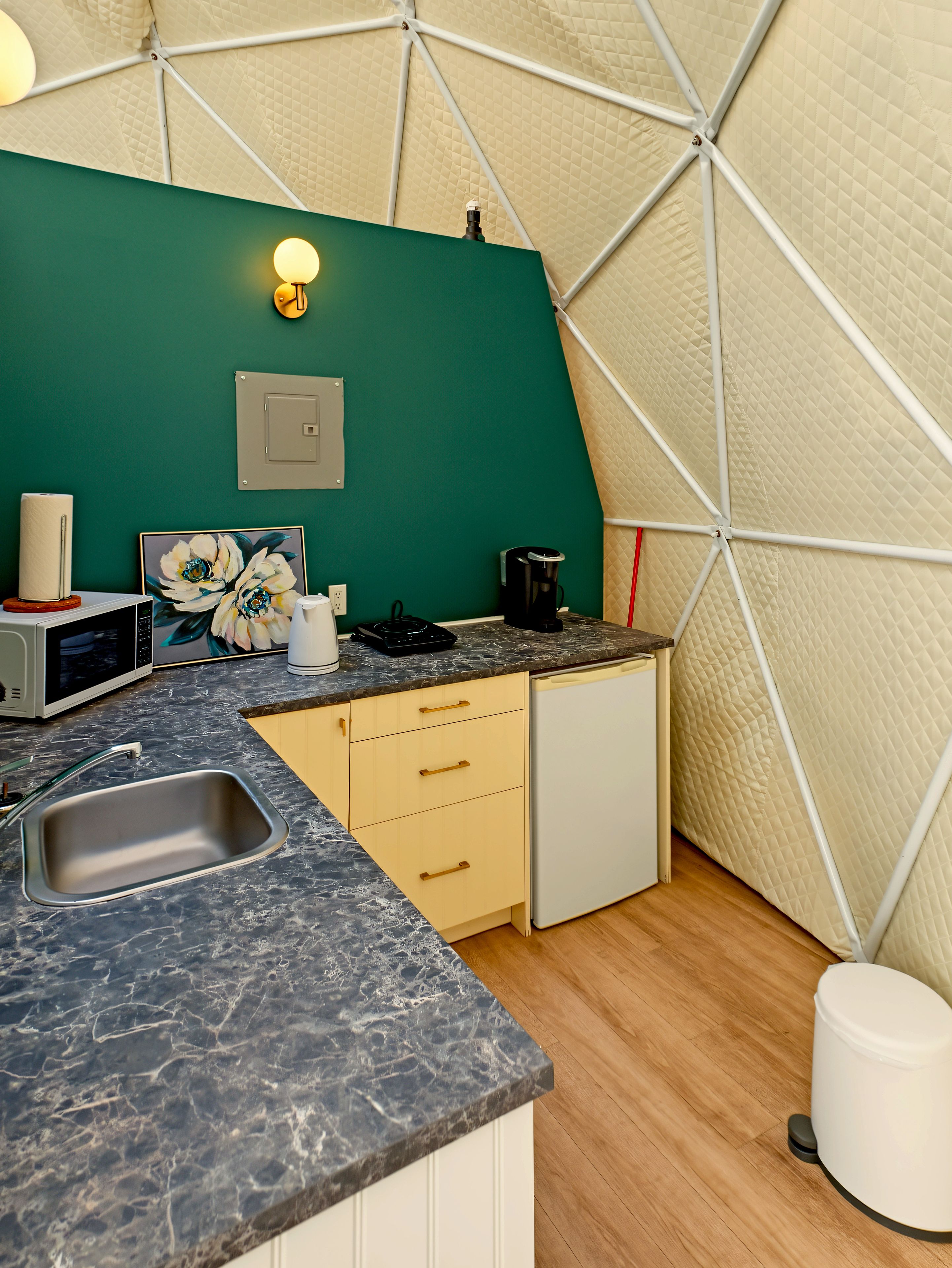 A compact kitchen with a sink, microwave, coffee maker, and a painting on the wall.