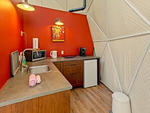 A compact kitchen with a microwave, kettle, coffee maker, and a small refrigerator. - Glamp Camp (Waterborough)