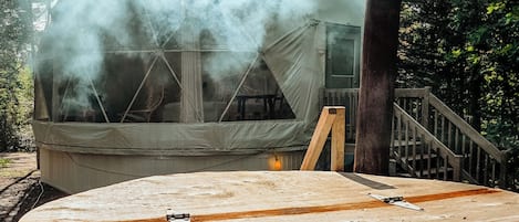 Een hottub met een houten terras, omringd door bomen, en een rookpluim in de verte.