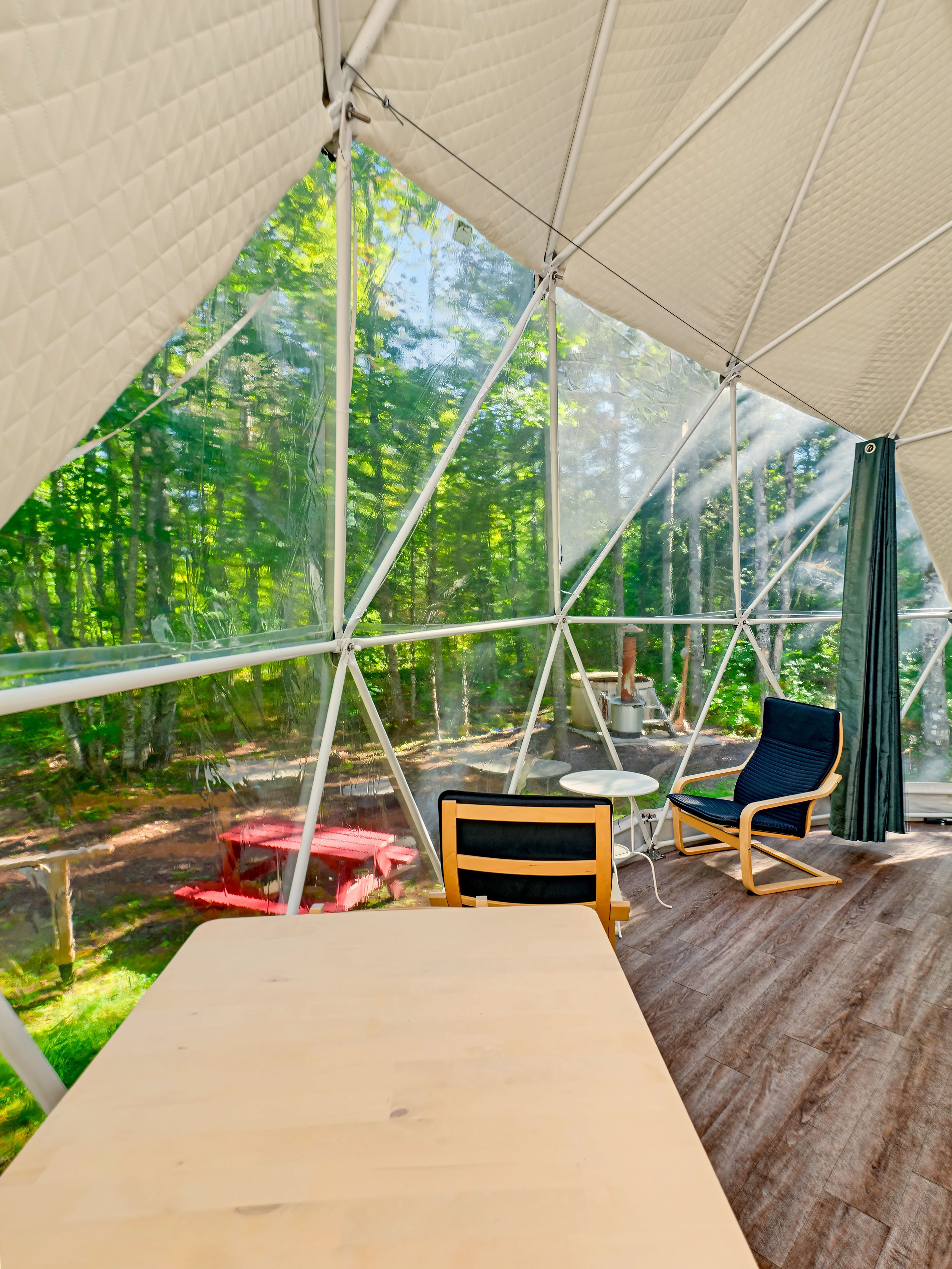 Un espace extérieur aménagé avec une tente, une table et des chaises, le tout entouré d’une vue sur la forêt.