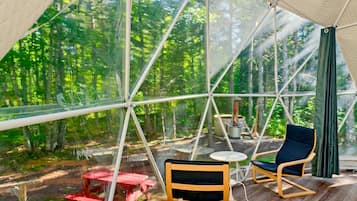 Un espace extérieur aménagé avec une tente, une table et des chaises, le tout entouré d’une vue sur la forêt.