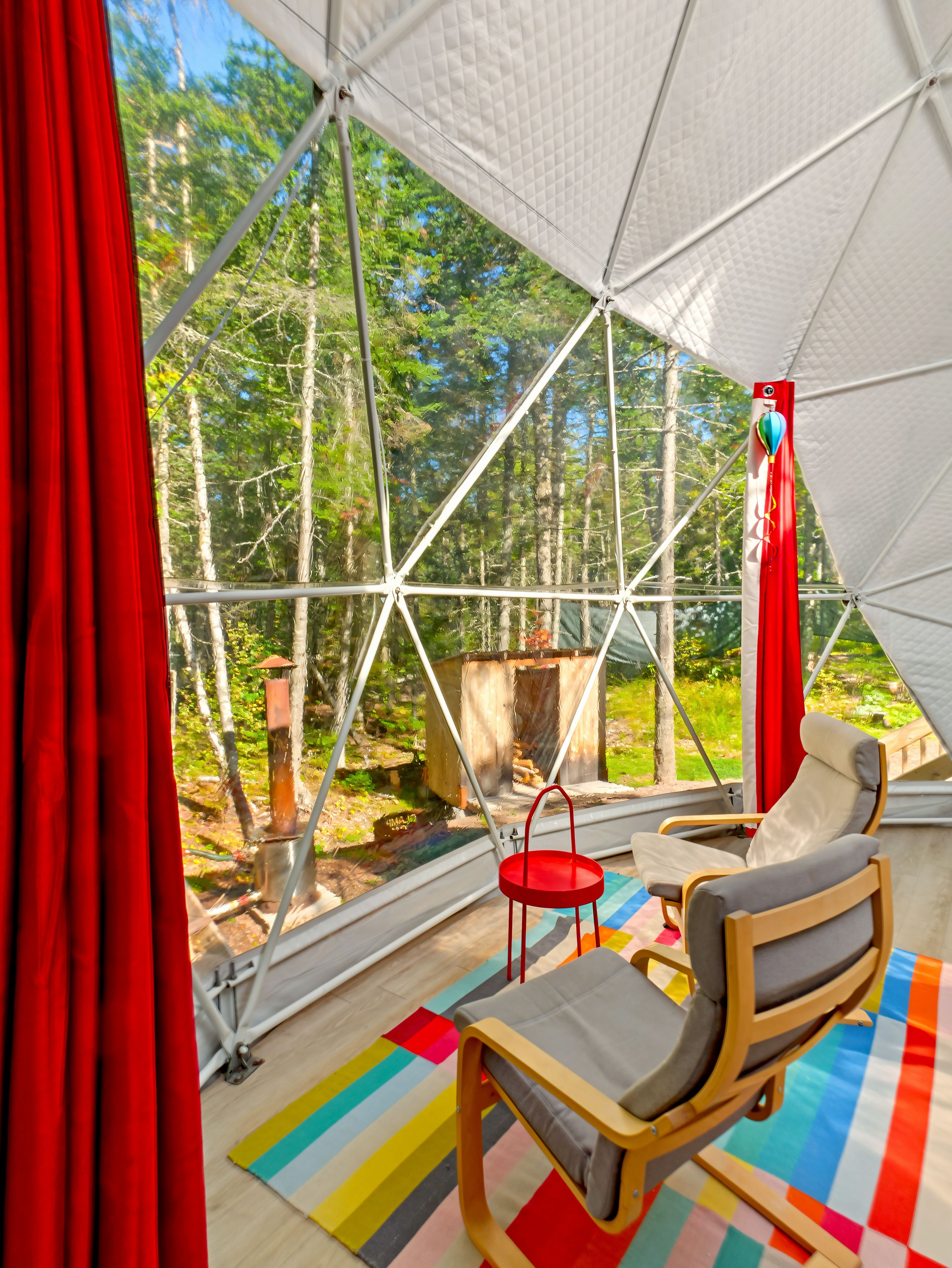 Een tent met uitzicht op een bos, een rode stoel en een kleurrijk tapijt.