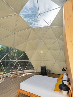 A room with a bed, a chair, a heater, and a window overlooking a forest. - Glamp Camp (Waterborough)