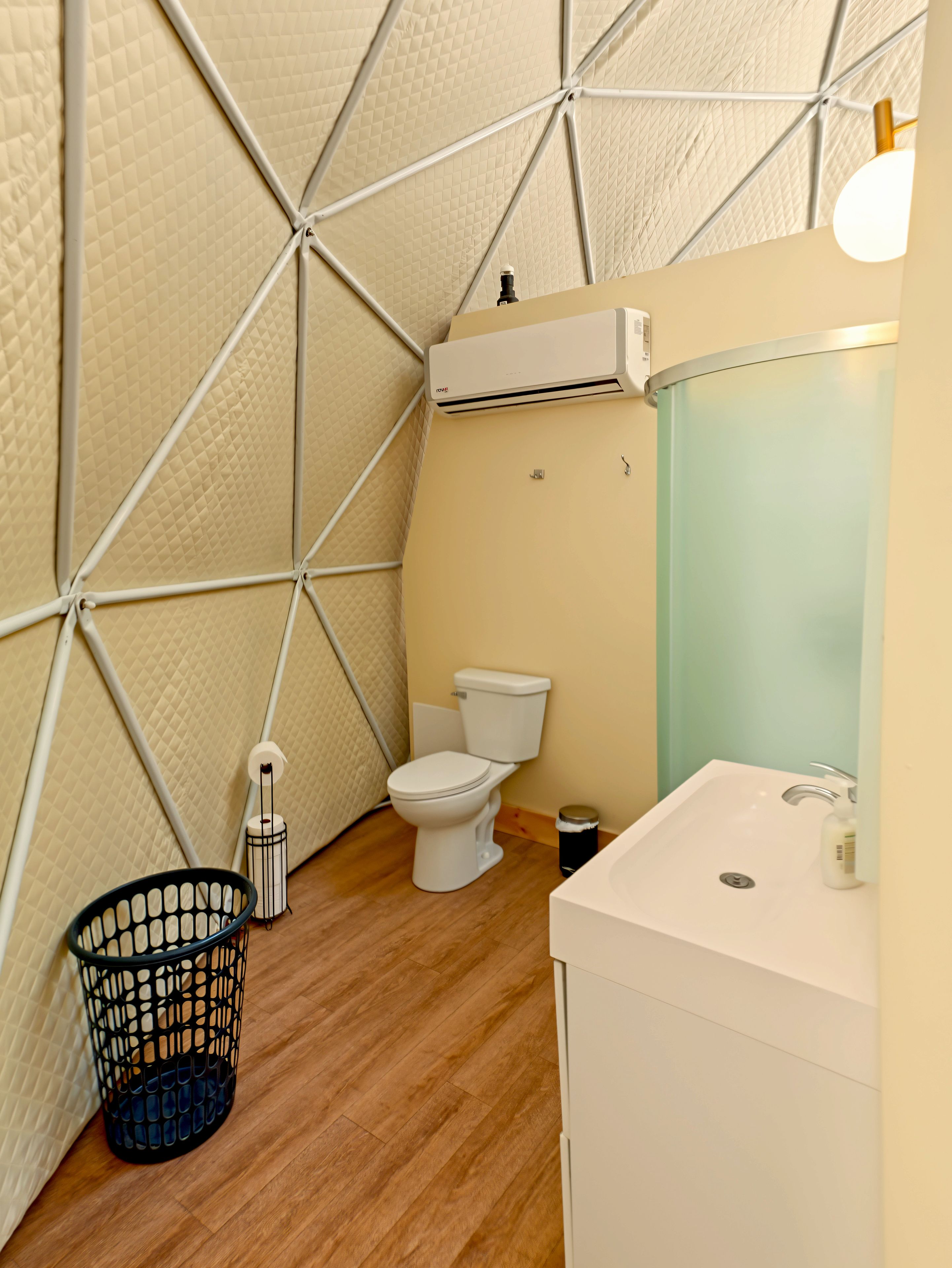 A compact bathroom with a white toilet, a white sink, and a black trash bin.