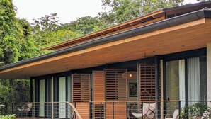 Uma casa moderna com um deck de madeira, janelas amplas e uma escadaria que leva a um andar superior.
