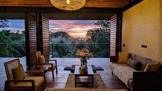 Espaço de estar aconchegante com vista para o pôr do sol e árvores.