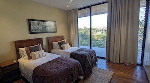 A bedroom with two beds, a large window with curtains, and a framed picture on the wall. - Casa Ibu 4 BR Jungle & Ocean View Luxury Villa with Private Pool and Gardens (Playa Santa Teresa)