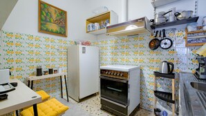 A kitchen with a refrigerator, oven, and various kitchen utensils. There is a painting on the wall and a shelf with kitchen items. - 4u Apartment Athens! 2 Minutes From Metro Station (Nea Ionia)