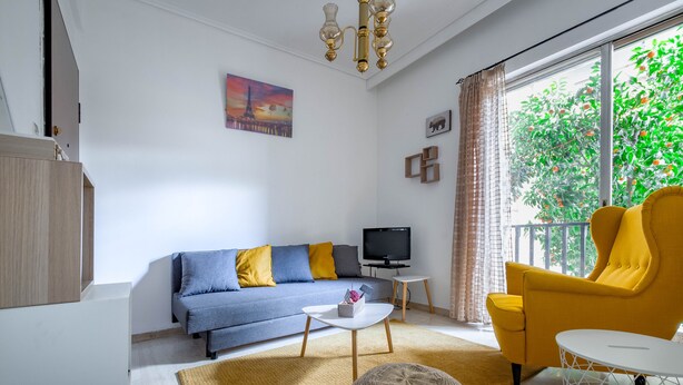 A modern living room with a sofa, a yellow armchair, a TV, and a large window with a view of trees. - 4u Apartment Athens! 2 Minutes From Metro Station (Nea Ionia)