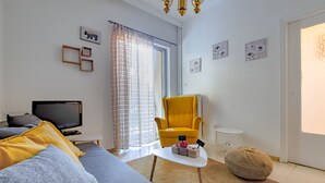 A modern living room with a sofa, a yellow armchair, a television, and a small table with a box labeled "Family." - 4u Apartment Athens! 2 Minutes From Metro Station (Nea Ionia)