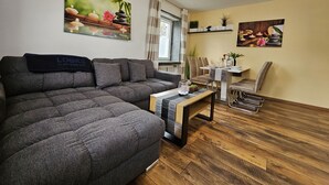 A modern living room with a grey sofa, a wooden coffee table, and a dining area with chairs and a small table. - Bright and modern apartment on the ground floor in the center (Kassel)