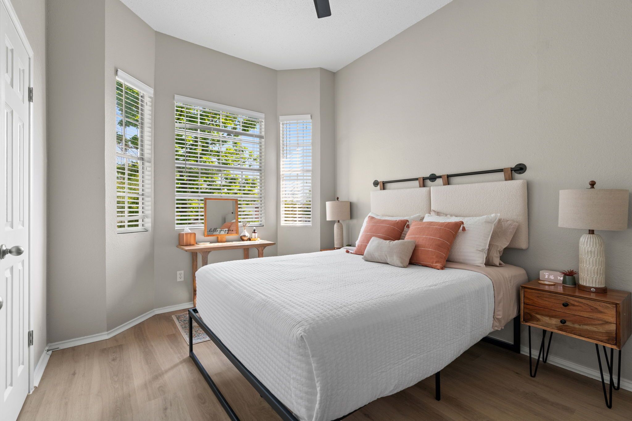 Quarto com cama, mesas de cabeceira, luminárias e janelas com persianas.
