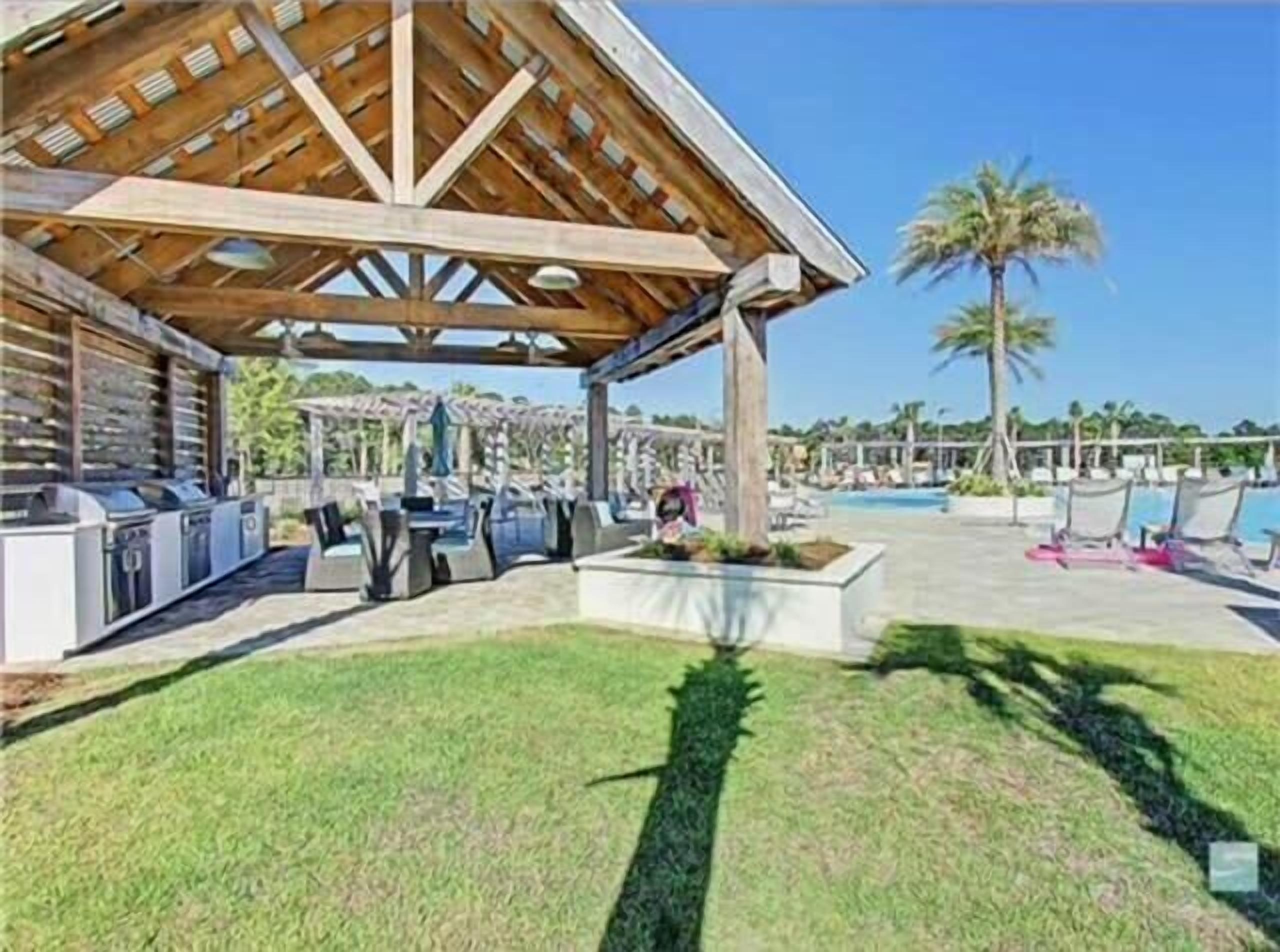 Un espacio al aire libre techado con una barbacoa, sillas de descanso y una piscina.