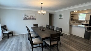 Un vaste espace dédié à la salle à manger, avec une longue table en bois et des chaises, un lustre et une cuisine en arrière-plan.