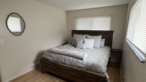 Une chambre avec un lit en bois, un miroir rond accroché au mur et une fenêtre avec des stores.