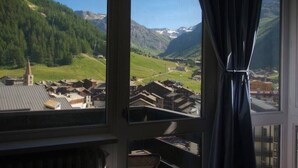 A room with a large window overlooking a mountainous landscape with a village below. - Very pretty apartment, well located, great view (Val-d'Isère)