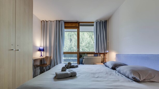 A bedroom with a bed, two bedside lamps, a window with curtains, and a radiator. - Very pretty apartment, well located, great view (Val-d'Isère)