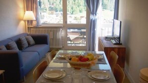 A dining area with a table set for four, a blue sofa, and a view of the outdoors. - Very pretty apartment, well located, great view (Val-d'Isère)