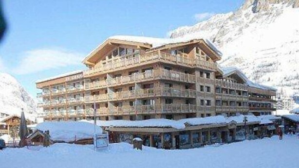 A multi-story hotel with balconies, surrounded by snow-covered mountains.