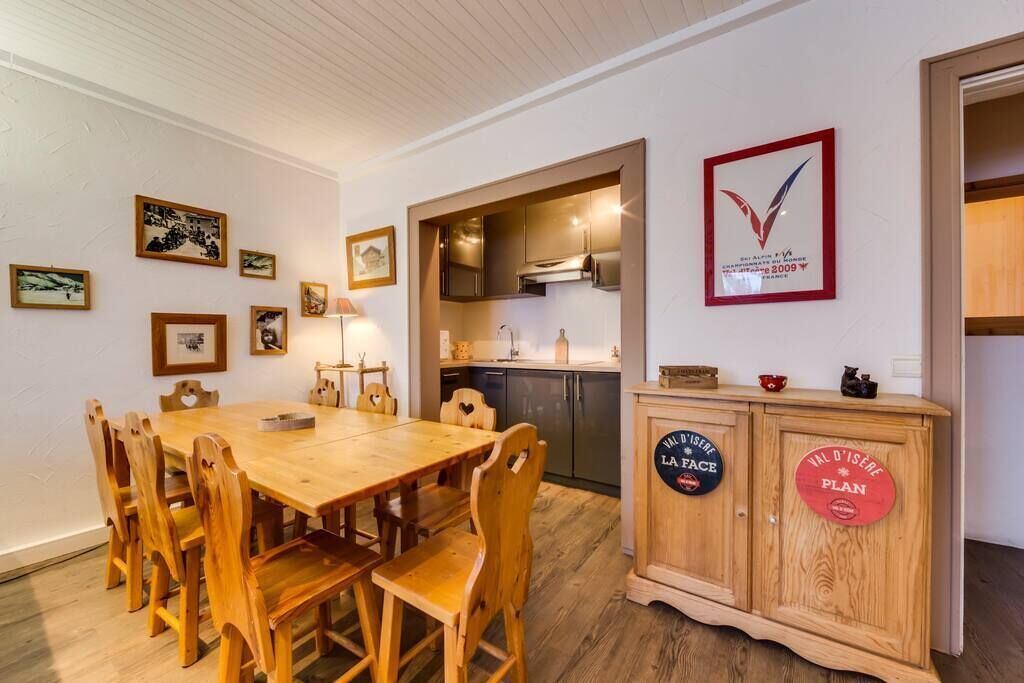 Et spiseområde med et træbord og stole, et køkken med moderne hårde hvidevarer, og et skab med dekorative skilte.