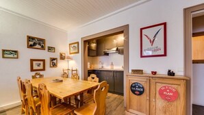 A dining area with a wooden table and chairs, a kitchen with modern appliances, and a cabinet with decorative signs.
