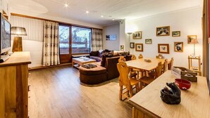 A cozy living room with a wooden dining table, comfortable seating, and a large window with curtains.