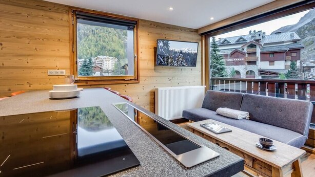 A modern kitchen with a large window, a built-in stove, and a seating area with a sofa and table.