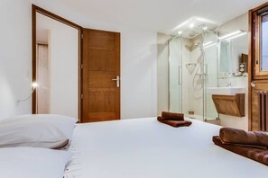 A bedroom with a wooden door, a glass shower enclosure, a white sink, and a large bed with white linens. - Beautiful 3 room apartment, 50m from ski slopes, RESIDENCE CROIX DU SUD (Val-d'Isère)