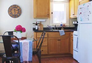 Compact kitchen with a dining area, featuring a refrigerator, a dining table, and a vase of flowers.