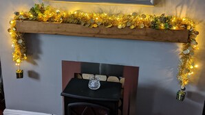 Una chimenea adornada con una guirnalda de luces, un pequeño árbol y un espejo encima.